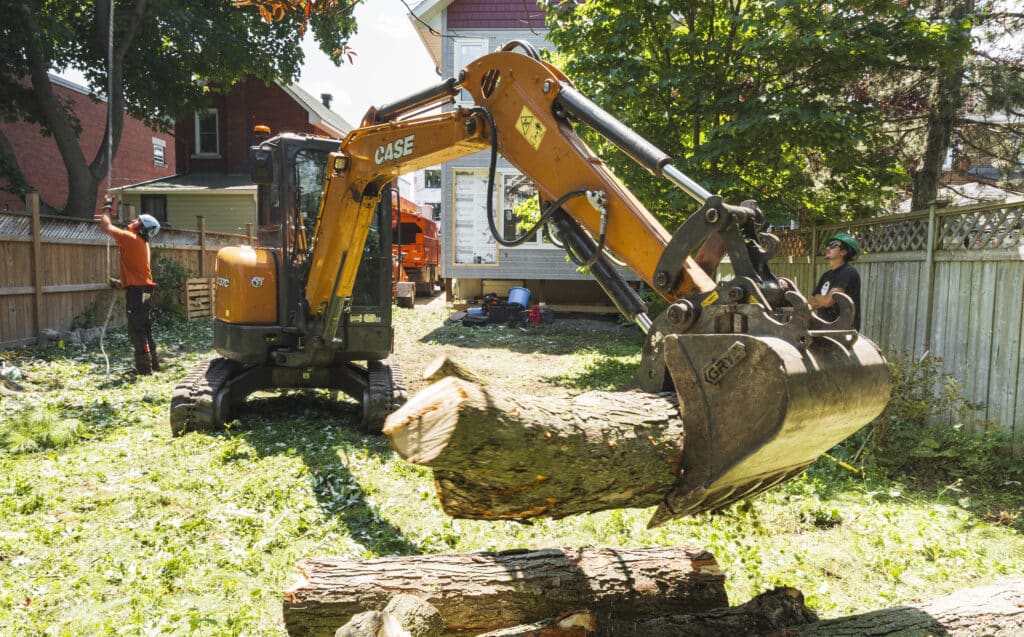 Excavator lifting a log during professional land clearing in Ottawa, with workers managing brush removal and site preparation.